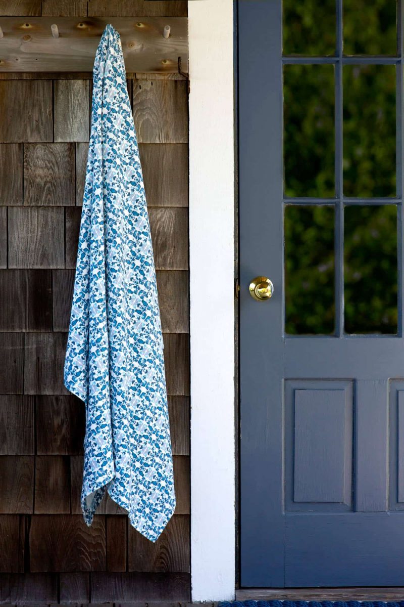Blue organic patterned knit blanket hanging on hook on cedar shingles next to a blue door