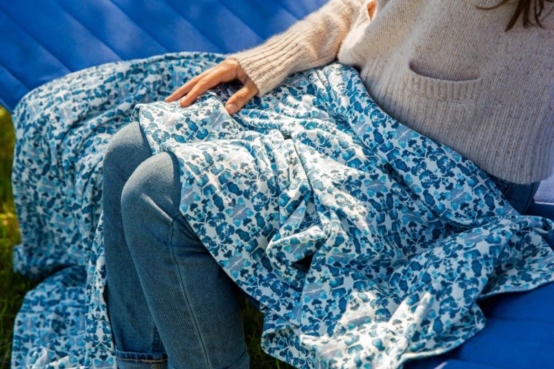 Luxury organic teal knit throw covering woman wearing a taupe sweater and blue jeans legs