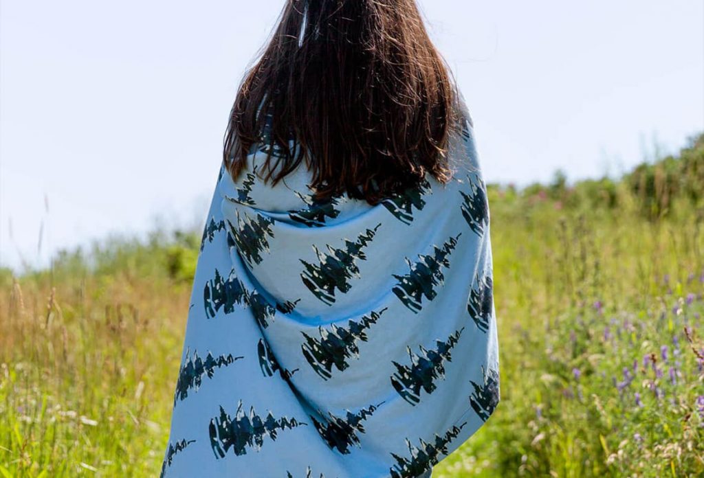 Brunette woman wrapped in a pine tree patterned blanket walking in a field