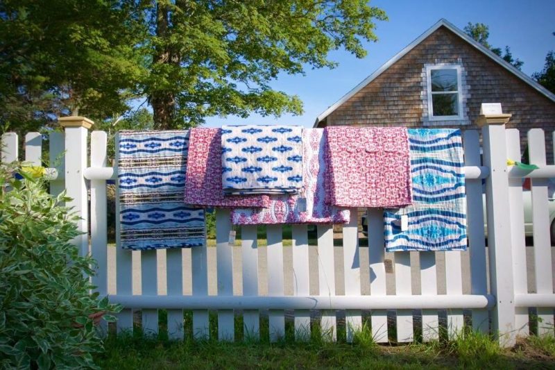 Handmade pink and blue organic quilts hanging outdoors on a white picket fence