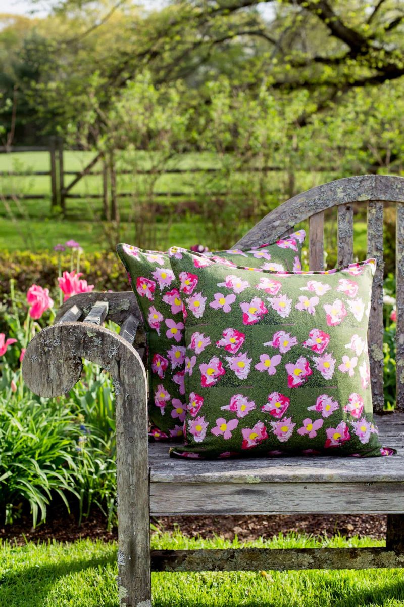 Two organic green floral pillows on a rustic bench in a garden