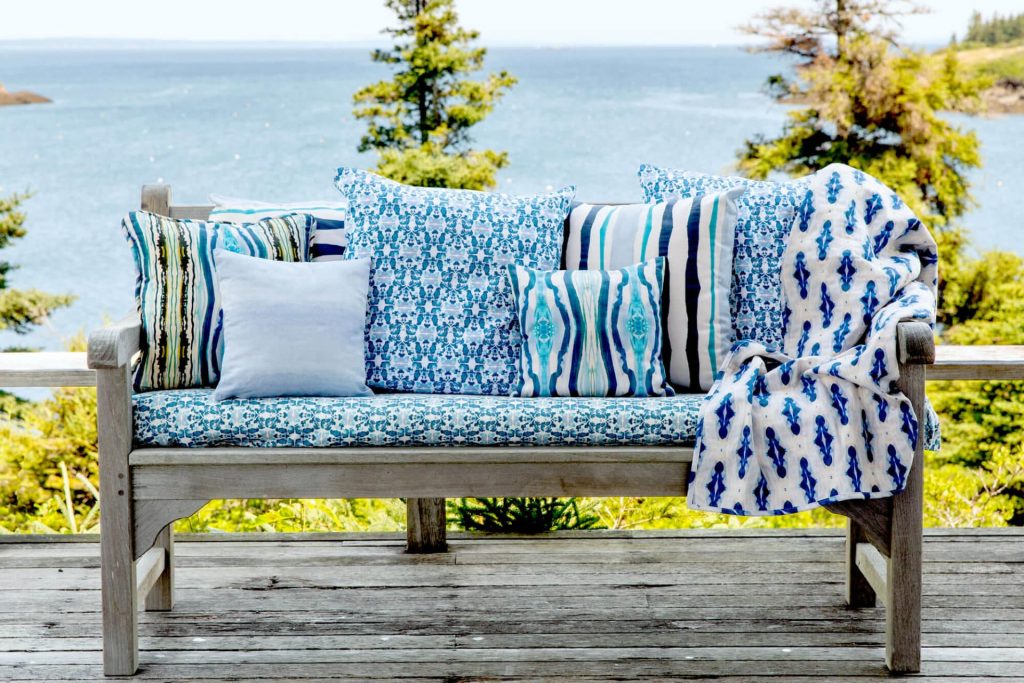 Organic blue pillows and blanket displayed on a rustic bench in front of the ocean