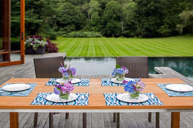 Poolside outdoor dining table setting with blue organic diamond placemats and flower arrangemnts