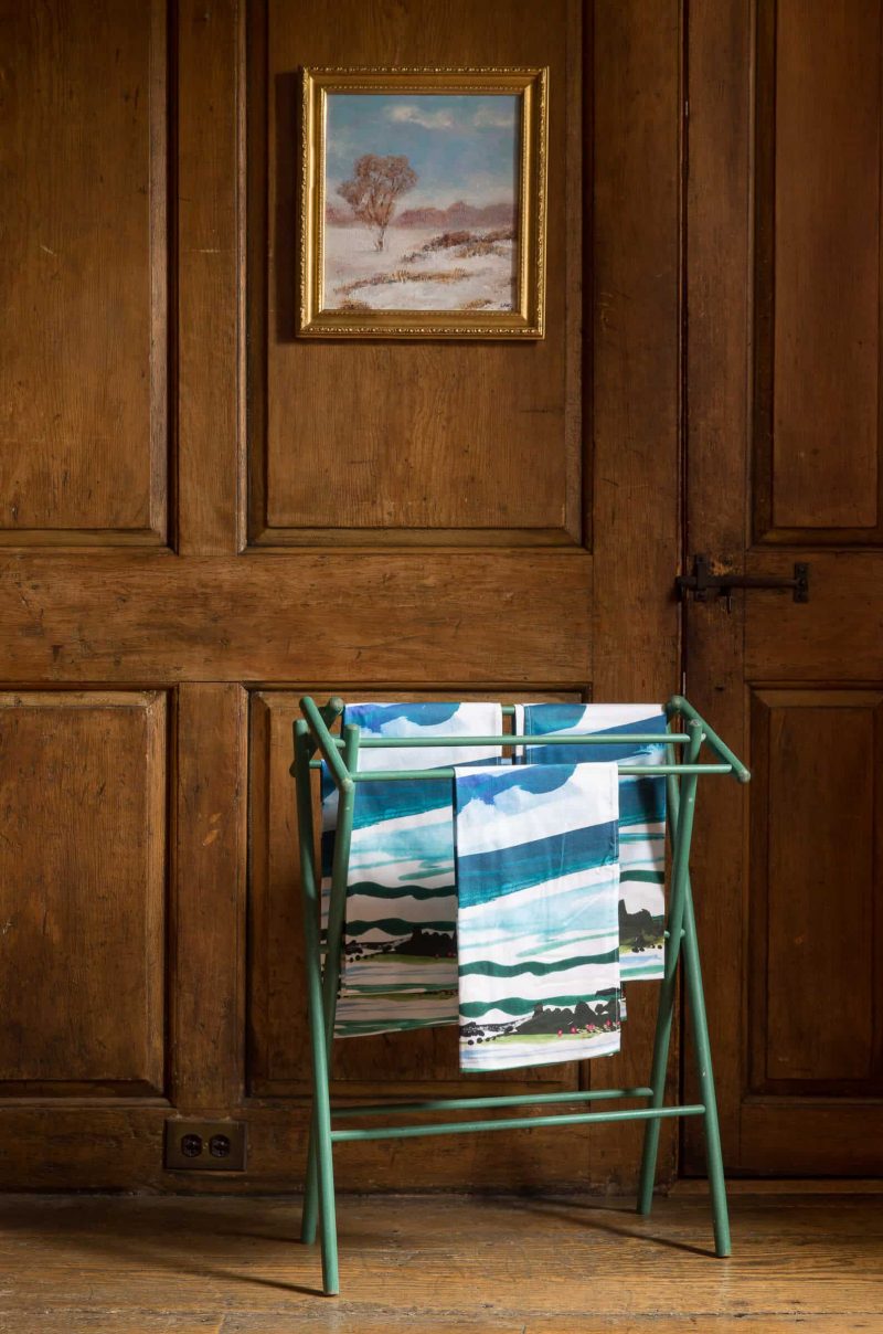 Luxury organic Maine watercolor painting kitchen tea towel hanging on a green drying rack in wood room