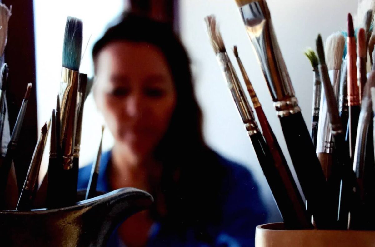 close up of cups of paintbrushes with blurred woman in background