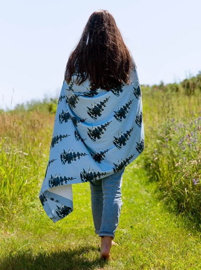 Brunette woman wrapped in a pine tree patterned blanket walking barefoot in a field