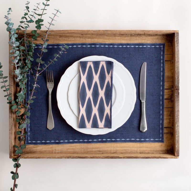 Navy and blush organic cotton napkin on solid blue placemat